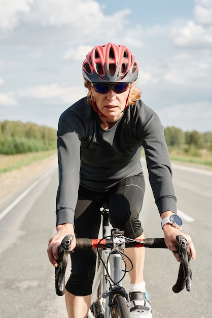 Retrato de atleta en casco montando en bicicleta a lo largo de la carretera durante su entrenamiento deportivo