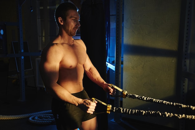 Foto retrato de un atleta de fitness con cuerpo musculoso hace ejercicios en equipos deportivos en el gimnasio, entrena los músculos del brazo, bombea bíceps y tríceps