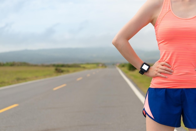 retrato de un atleta profesional que usa un reloj inteligente de frecuencia cardíaca deportiva para hacer ejercicio y probar los mejores resultados personales a través de productos tecnológicos en el fondo de la carretera.