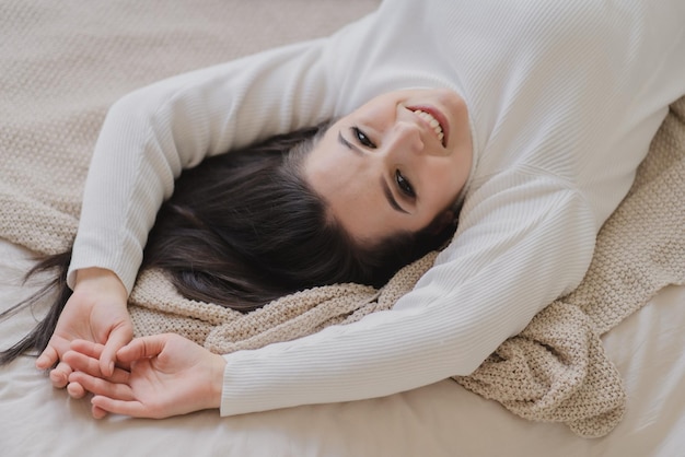 Retrato de una atractiva chica alegre de blanco acostada en la cama con una pose relajante y buen humor