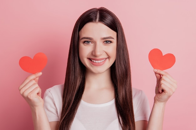 Retrato de atractiva chica bastante alegre sosteniendo en las manos pequeño corazón día de San Valentín aislado sobre fondo de color rosa