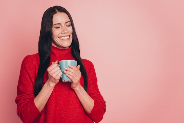 Retrato de una atractiva chica morena en suéter casual sosteniendo una taza de café aislado sobre fondo de color rosa