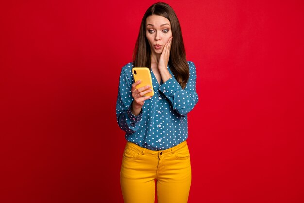 Retrato de una atractiva chica sorprendida utilizando la navegación celular comentarios de noticias smm puchero labios aislados sobre fondo de color rojo brillante