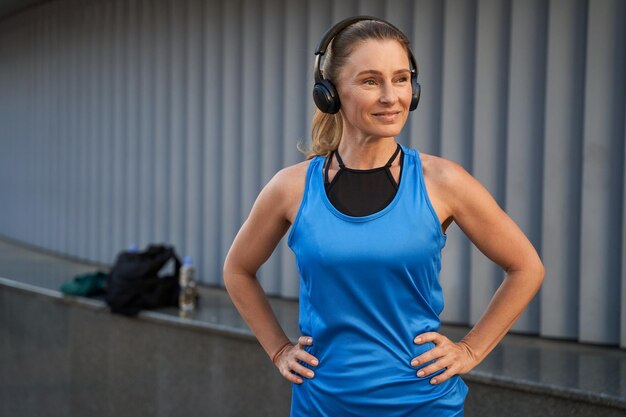 Retrato de atractiva deportista de mediana edad en ropa deportiva y auriculares sonriendo escuchando