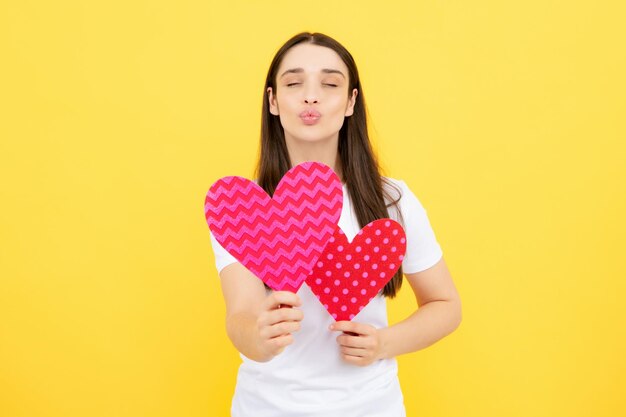 Retrato de una atractiva y encantadora chica alegre sosteniendo en las manos un corazón de papel aislado sobre amarillo