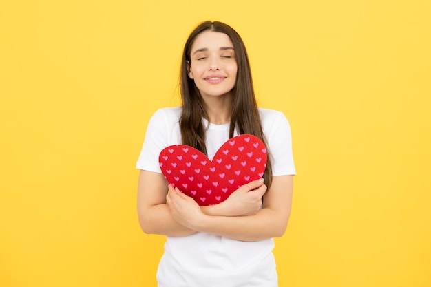 Retrato de una atractiva y encantadora chica alegre sosteniendo en las manos un corazón de papel aislado sobre un fondo amarillo San Valentín amor y belleza