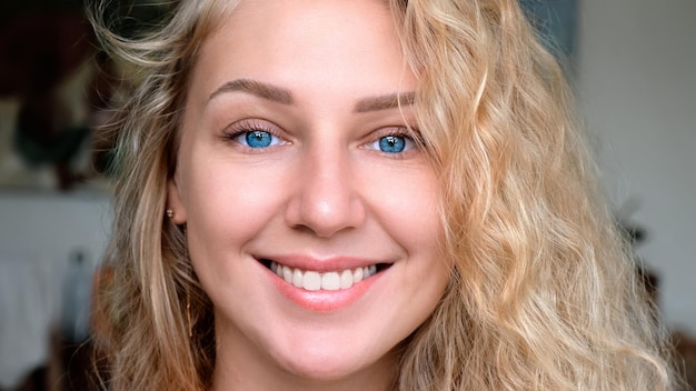 Foto retrato de una atractiva y encantadora mujer joven sonriente con cabello blanco rizado y ojos azules que miran hacia mí