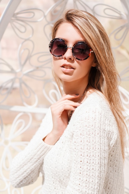 Retrato de una atractiva joven hipster en un suéter vintage de moda en elegantes gafas de sol redondas en