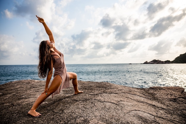 Un retrato de una atractiva joven practicando yoga junto al mar al amanecer.