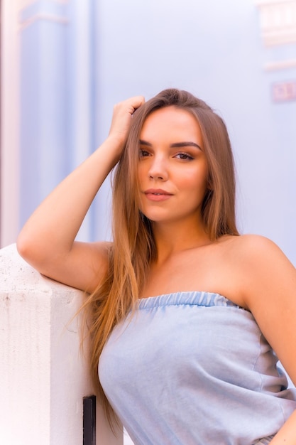 Retrato de una atractiva joven rubia con peto azul sonriendo en una casa azul