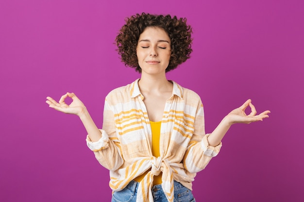 Retrato de una atractiva joven sonriente con cabello rizado morena que se encuentran aisladas sobre la pared violeta, meditando