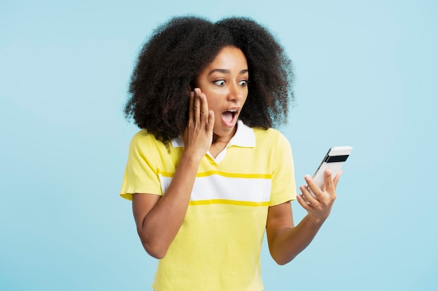 Retrato de una atractiva mujer afroamericana emocionada con ropa informal sosteniendo un teléfono móvil