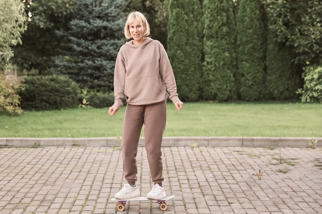 Retrato de una atractiva mujer alegre aprendiendo a patinar en monopatín pasando el fin de semana al aire libre