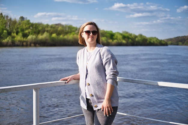 Retrato de una atractiva mujer caucásica con gafas de sol en un muelle junto al río en un cálido día soleado de verano