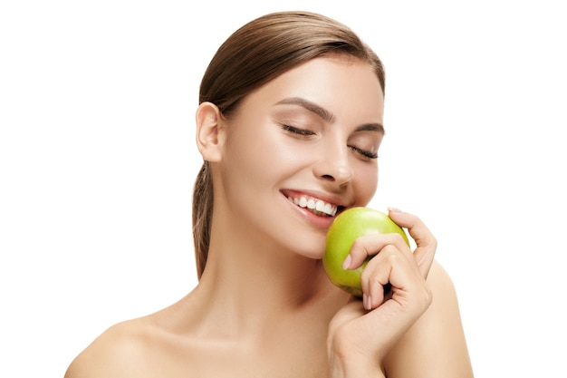 El retrato de la atractiva mujer caucásica sonriente aislada en la pared blanca con frutos de manzana verde. La belleza, cuidado, piel, tratamiento, salud, spa, cosmética