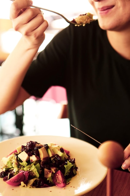 Retrato de una atractiva mujer caucásica sonriente comiendo ensalada centrada en la mano y el tenedor