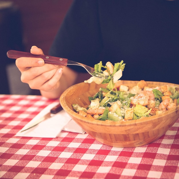 Retrato de una atractiva mujer caucásica sonriente comiendo ensalada centrada en la mano y el tenedor