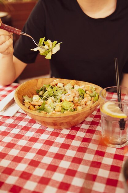 Retrato de una atractiva mujer caucásica sonriente comiendo ensalada centrada en la mano y el tenedor