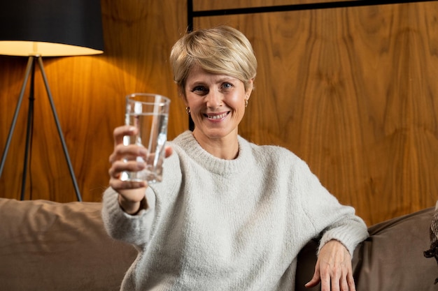 Retrato de una atractiva mujer de mediana edad alegre sosteniendo un vaso de agua limpia sentado en el