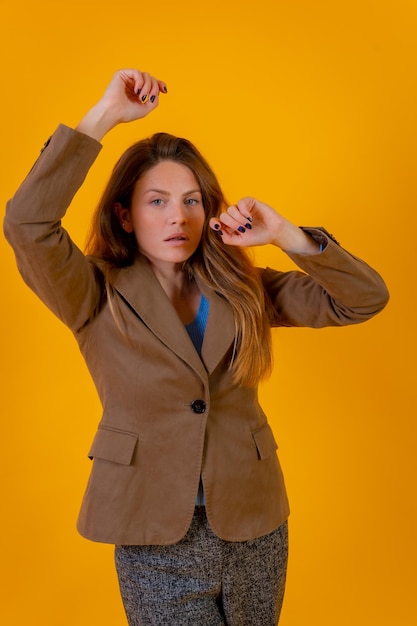 Retrato de una atractiva mujer de ojos azules sobre un fondo amarillo en un concepto de moda de chaqueta marrón
