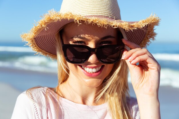 Retrato de una atractiva mujer rubia caucásica disfrutando del tiempo en la playa en un día soleado, mirando la cámara y sonriendo, con el cielo azul y el mar de fondo. Vacaciones de verano en la playa tropical.