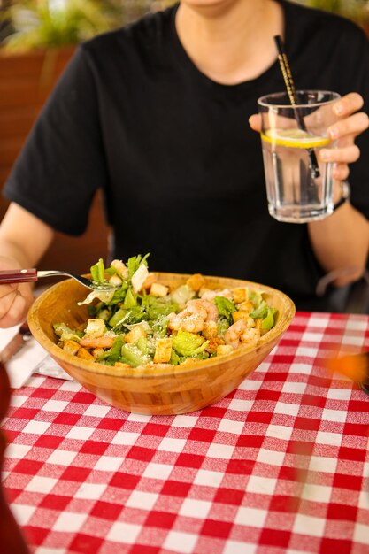 Retrato de una atractiva mujer sonriente caucásica comiendo ensalada, concentrándose en la mano y el tenedor.