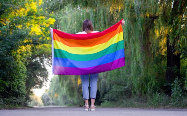 Retrato de una atractiva mujer sosteniendo una bandera gay LGBT arco iris sobre sus hombros, mirando hacia un lado.