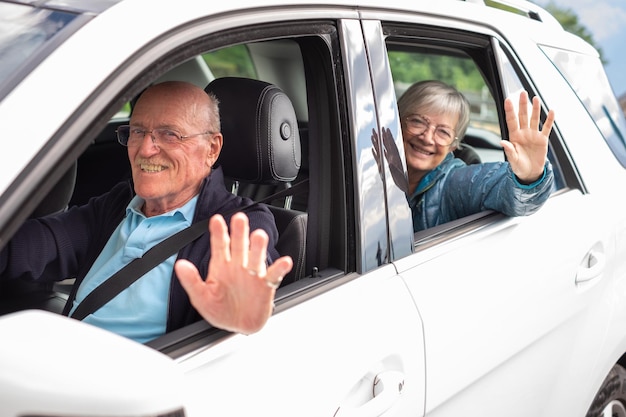 Retrato de una atractiva pareja de ancianos feliz sentada en el coche, un hombre listo para conducir mirando a la cámara sonriendo