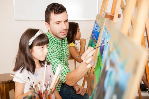 Retrato de una atractiva profesora de arte hispana ayudando a una niña con su pintura