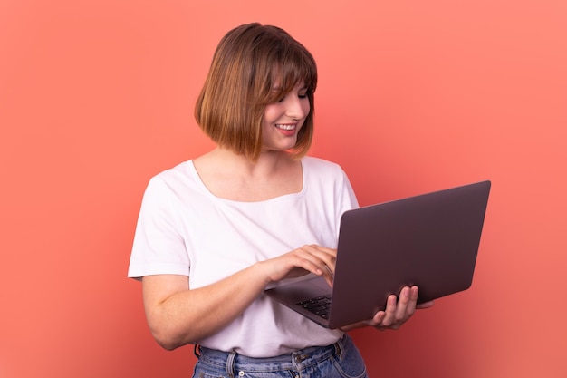 Retrato atractivo corredor de agente de chica alegre asombrada usando una computadora portátil divirtiéndose fondo de color rosa