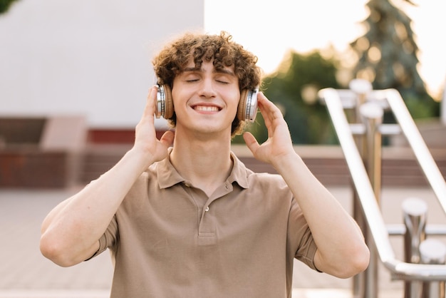 Retrato de atractivo estudiante varón de pelo rizado en auriculares sonriendo