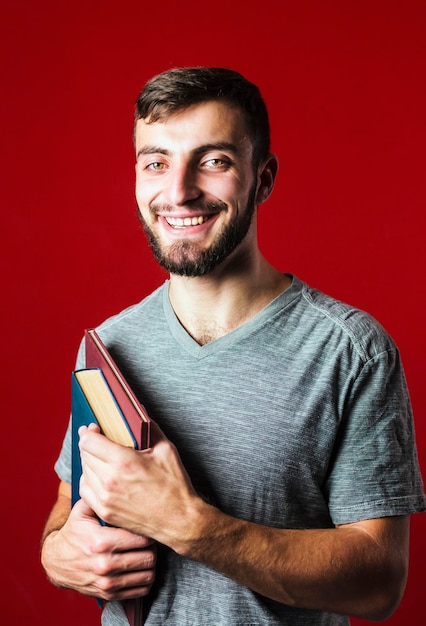 Un retrato de un atractivo y guapo estudiante sonriente con barba y libros de fondo rojo