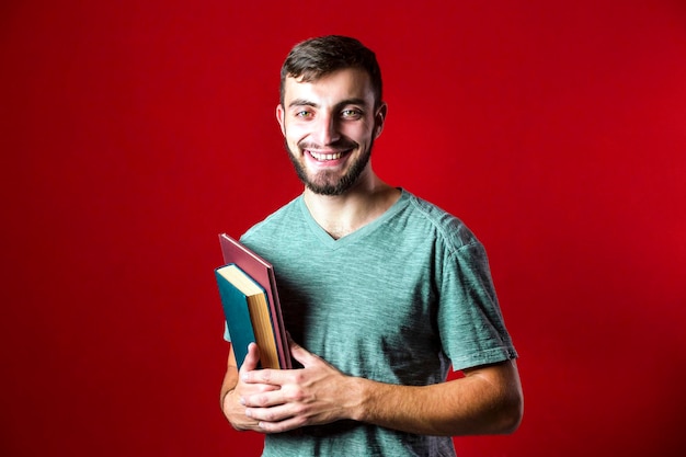Un retrato de un atractivo y guapo estudiante sonriente con barba y libros de fondo rojo