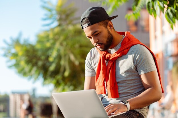 Foto retrato de un atractivo hombre afroamericano usando una computadora portátil sentado al aire libre en el parque