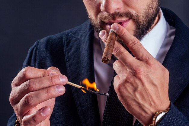 Retrato de un atractivo hombre de negocios con un cigarro en un estudio de fondo negro