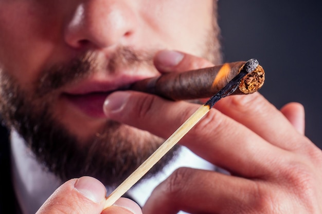 Retrato de un atractivo hombre de negocios con un cigarro en un estudio de fondo negro