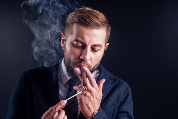 Retrato de un atractivo hombre de negocios con un cigarro en un estudio de fondo negro
