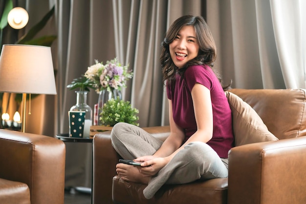 Retrato atractivo inteligente mujer asiática adulta cabello largo negro casual sonriendo en la sala de estar en el sofá con frescura alegre y expresión de emoción positiva distancia trabajando desde el concepto de hogar