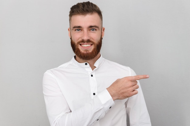 Retrato de un atractivo joven empresario de pie sobre una pared gris, apuntando con el dedo hacia el espacio de la copia