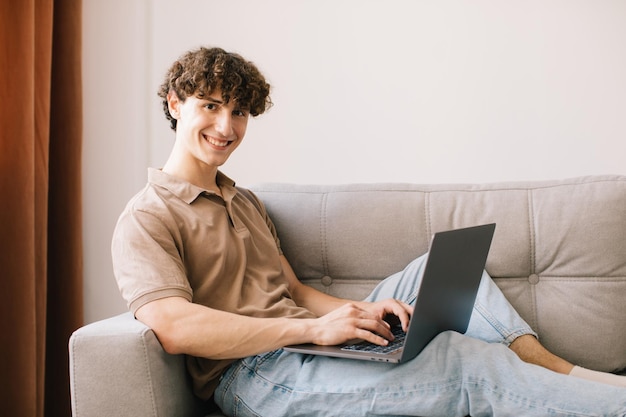 Retrato de un atractivo joven de pelo rizado que usa una laptop mientras se sienta en el sofá en casa