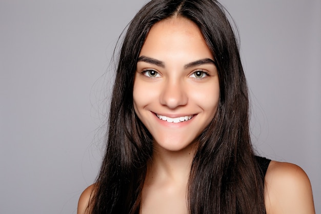 Retrato de un atractivo sonriente mirando a la cámara. Llevaba un vestido negro. Posando sobre fondo gris. Hermosa mujer sonriente con piel limpia, maquillaje natural y dientes blancos