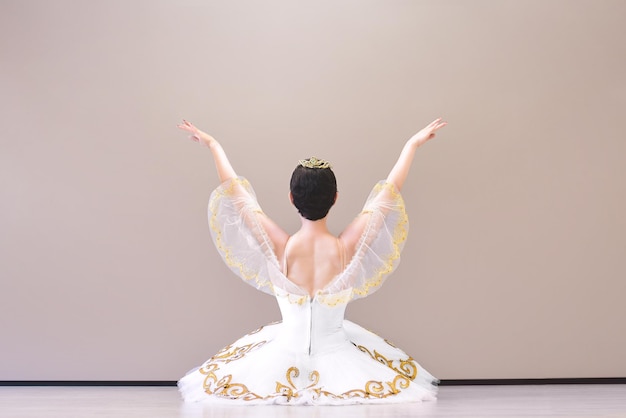 Retrato desde atrás de una encantadora bailarina sentada en el suelo en el salón de baile calentándose antes de la actuación