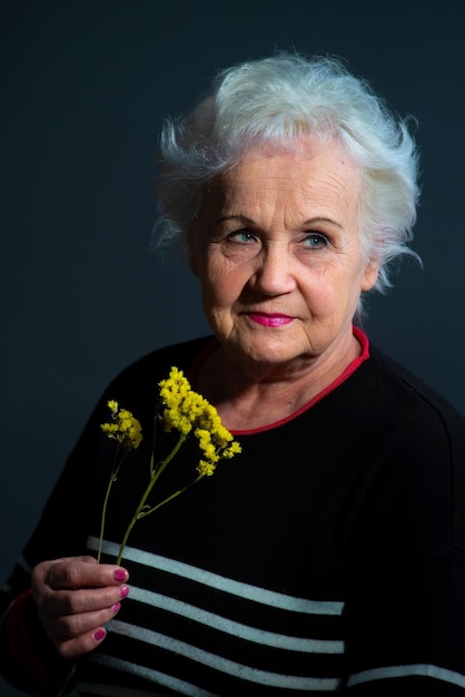 Retrato autêntico da avó segurando flor amarela em fundo cinza escuro