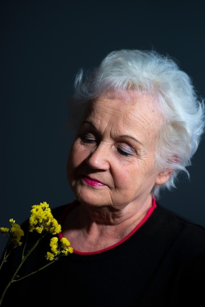 Retrato autêntico da avó segurando flor amarela em fundo cinza escuro