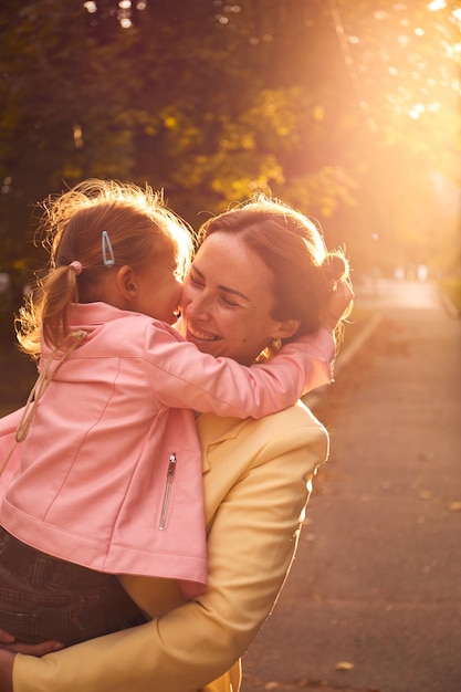 Foto retrato auténtico de la madre y su hija en el parque de otoño durante la puesta de sol disfrutando del tiempo juntos