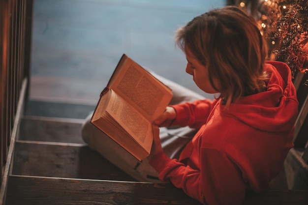 Retrato de un auténtico niño sonriente sincero leyendo un libro sobre la distancia estudiando en casa Navidad