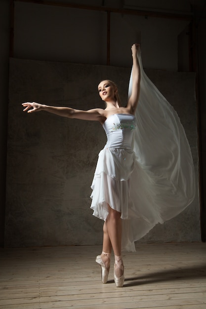 Retrato de bailarina de ballet rubia con los brazos arriba bailando en pointes en estudio