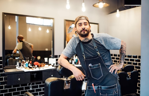 Foto retrato de un barbero apoyado en una silla en el salón