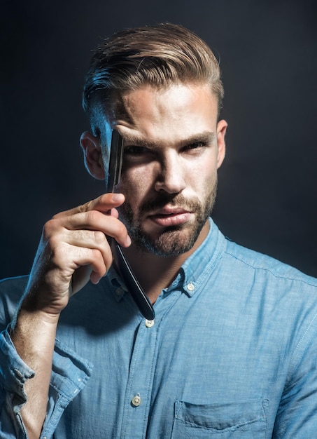 Retrato barbudo bonito segurando uma lâmina perigosa perto do rosto de um jovem com barba e bigode