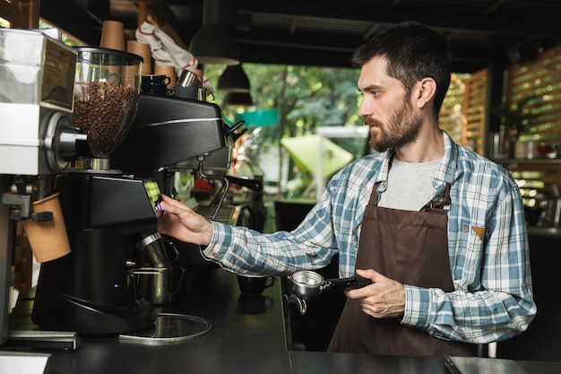 Retrato de barista serio hombre vestido con delantal haciendo café mientras trabajaba en la cafetería de la calle o al aire libre en una cafetería